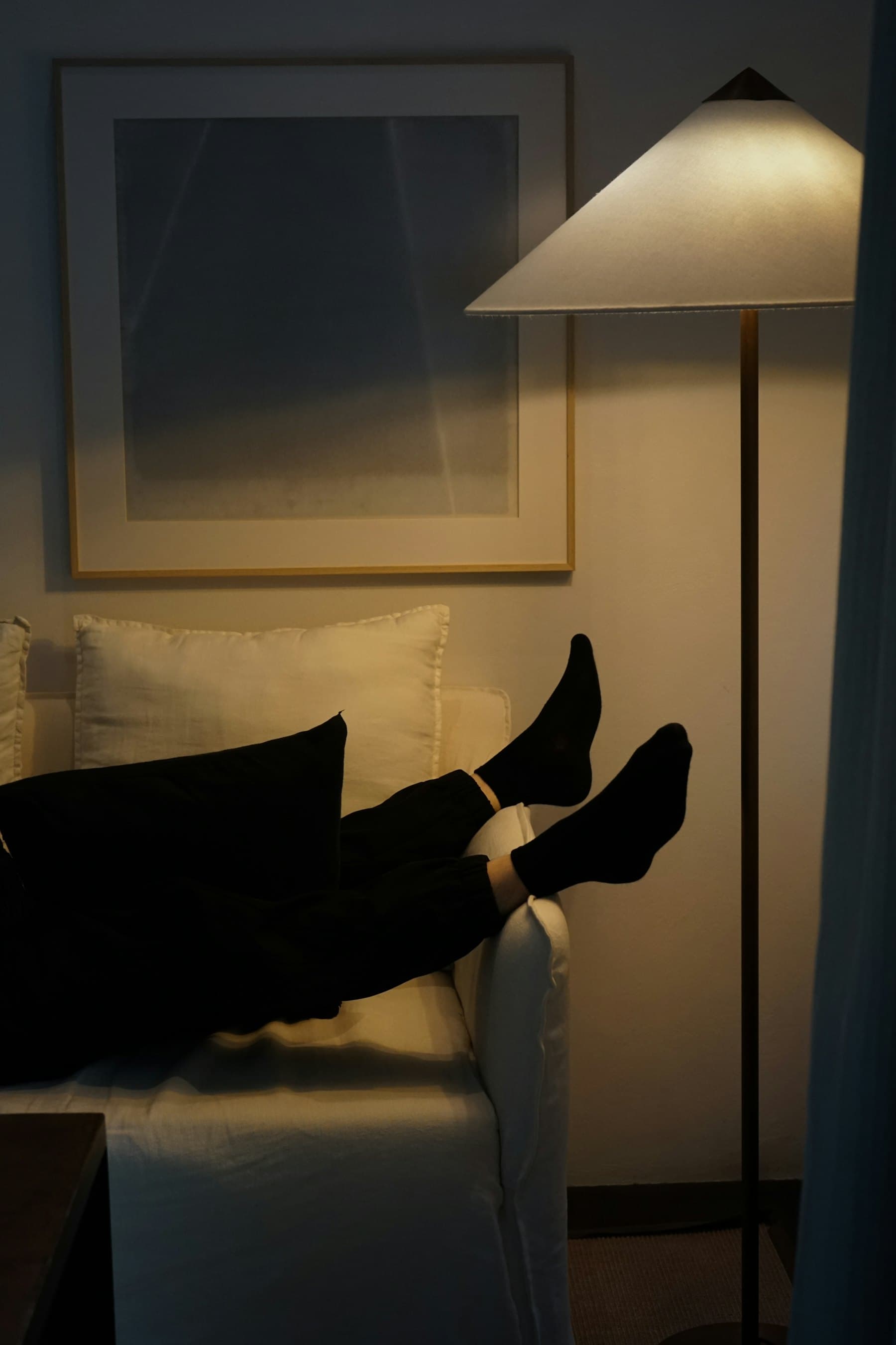 Someone relaxing on a sofa in a warm, lamp-lit room